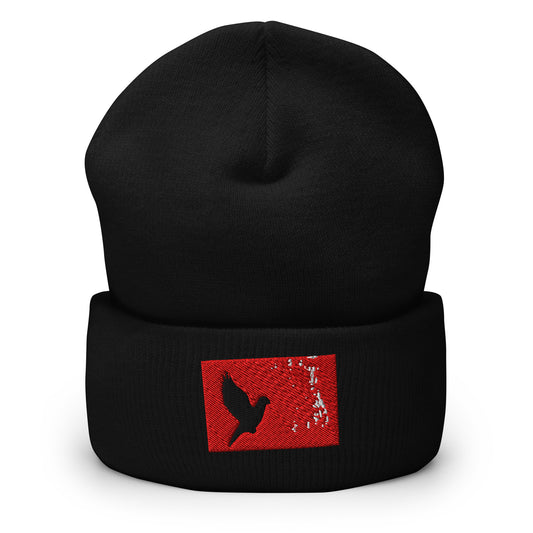 Black cuffed beanie with an embroidered design. Black bird flying with a red rectangle behind it and white splatters against the red rectangle.