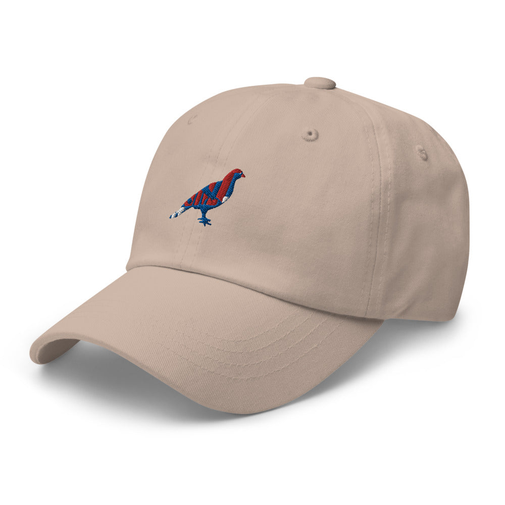 Beige dad hat with an embroidered blue, red, and white pigeon. Hat is turned to it's left.
