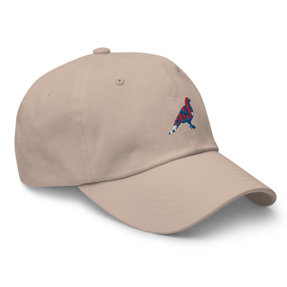 Beige dad hat with an embroidered blue, red, and white pigeon. Hat is turned to it's right.