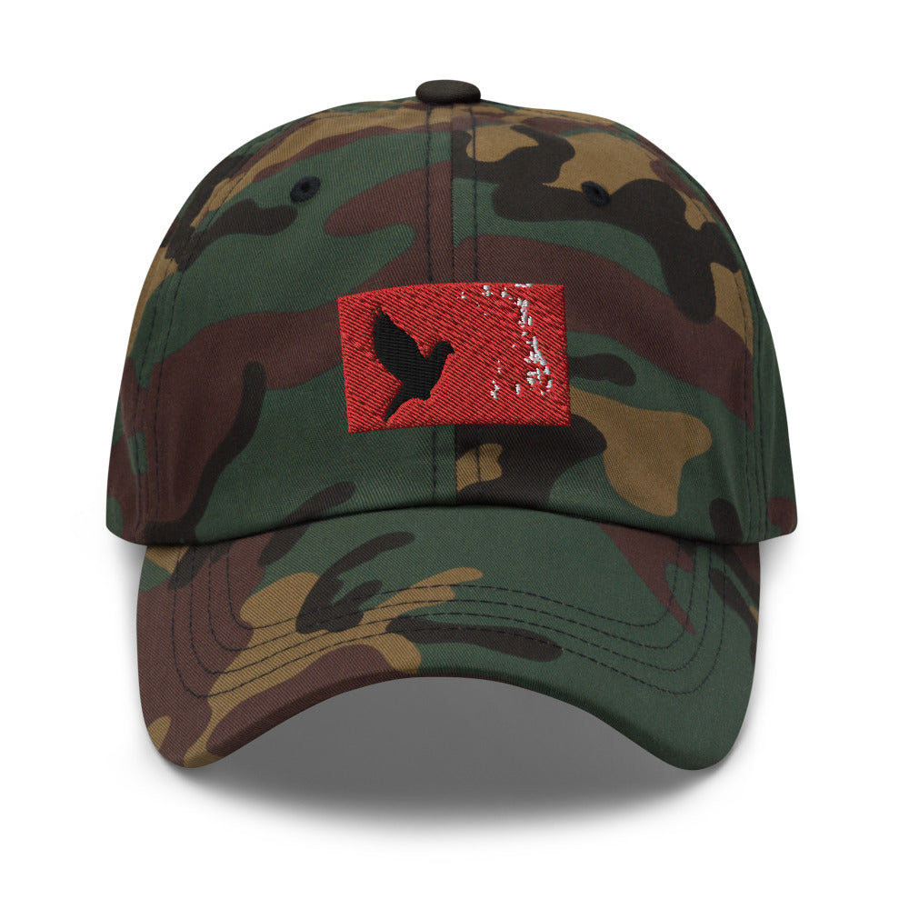 Camouflage dad hat with an embroidered red rectangle and a black pigeon flying on it.