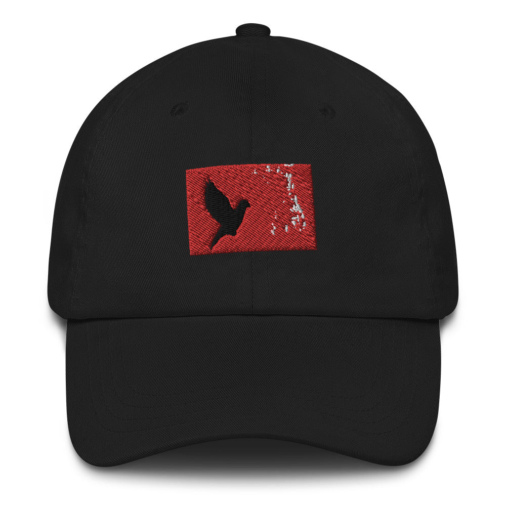 Black dad hat with an embroidered red rectangle and a black pigeon flying on it. Close up pic.